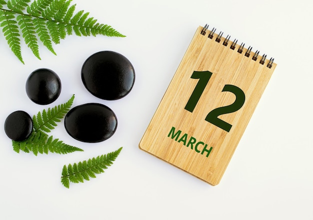 Zdjęcie 12 marca 12 dzień miesiąca data kalendarzowa notatnik czarne kamienie zielone liście wiosenny miesiąc pojęcie dnia roku