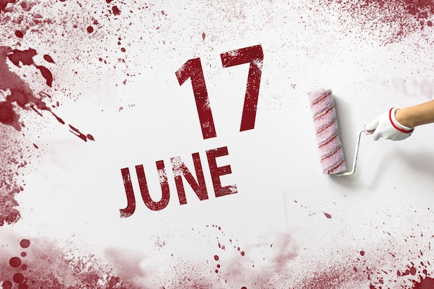 17 czerwca. Dzień 17 miesiąca, data kalendarzowa. Ręka trzyma wałek z czerwoną farbą i pisze datę w kalendarzu na białym tle. Miesiąc letni, koncepcja dnia roku.