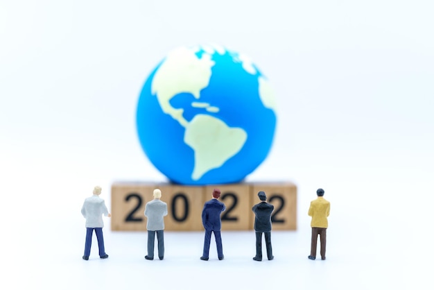 2022 nowy rok i koncepcja planowania biznesowego zbliżenie grupy miniaturowe figurki biznesmena stojącego i patrzącego na drewniany blok numeryczny z mini kulą światową na białym tle