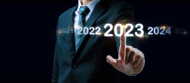 Zdjęcie 2023 ręka biznesmena dotykająca i wskazująca na rok 2023 z wirtualnym ekranem na ciemnym tle cel zmiana celu od 2022 do 2023 strategia inwestycje planowanie biznesowe koncepcja szczęśliwego nowego roku