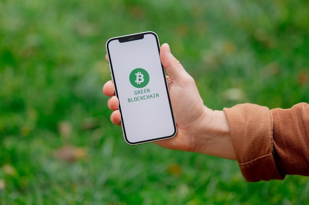 23 listopada 2021 - Wrocław, Polska: Mężczyzna trzyma iPhone'a z zielonym logo eco bitcoin i tekstem blockchain. Trend 2022 roku