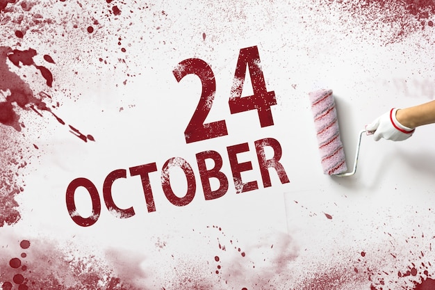 24 października. 24 dzień miesiąca, data kalendarzowa. Ręka trzyma wałek z czerwoną farbą i pisze datę w kalendarzu na białym tle. Jesienny miesiąc, koncepcja dnia roku.
