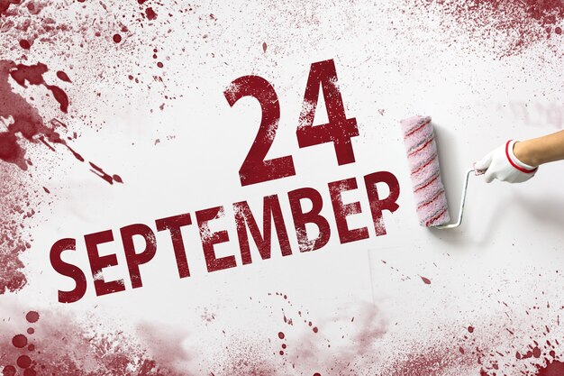 24 września. 24 dzień miesiąca, data kalendarzowa. Ręka trzyma wałek z czerwoną farbą i pisze datę w kalendarzu na białym tle. Jesienny miesiąc, koncepcja dnia roku.