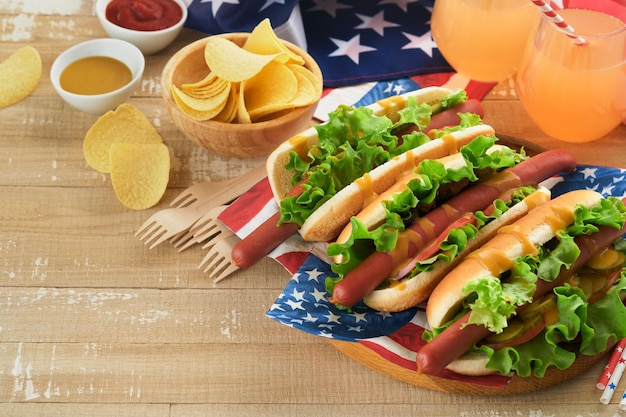 4 lipca Amerykański Dzień Niepodległości tradycyjne jedzenie piknikowe Hot dog z chipsami ziemniaczanymi i koktajlem Amerykańskie flagi i symbole USA Patriotyczne święto piknikowe na drewnianym tle Widok z góry