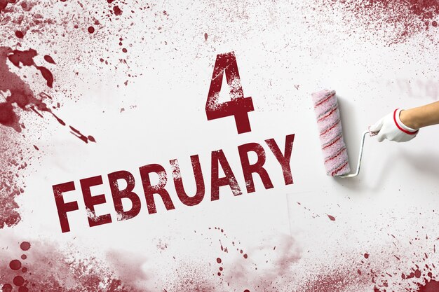 Zdjęcie 4 lutego. dzień 4 miesiąca, data kalendarzowa. ręka trzyma wałek z czerwoną farbą i pisze datę w kalendarzu na białym tle. miesiąc zimowy, koncepcja dnia roku.
