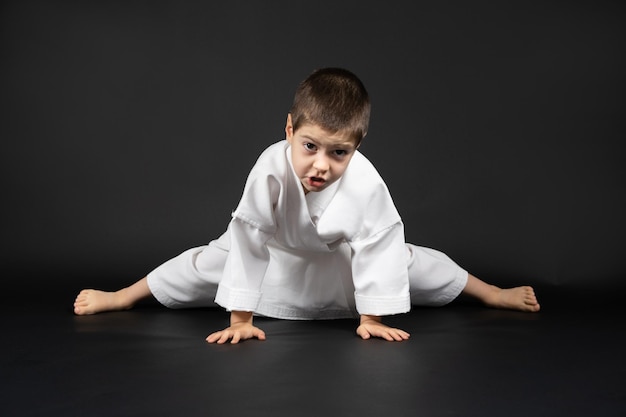 5-letni chłopiec ćwiczy karate rozciąga nogi na czarnym tle Przygotowanie do treningu rozciągania mięśni