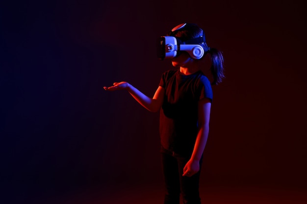 5-letnia dziewczynka przeżywa grę VR na kolorowej powierzchni. Dziecko korzystające z gadżetu do gier w wirtualnej rzeczywistości. Futurystyczne okulary w młodym wieku. Technologia wirtualna.