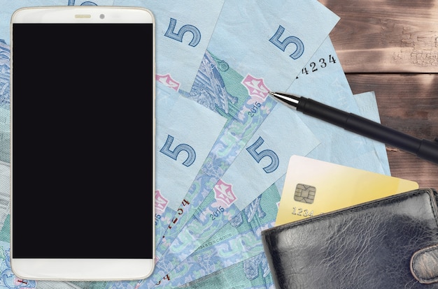 5 rachunków w hrywnach ukraińskich oraz smartfon z torebką i kartą kredytową. E-płatności lub koncepcja e-commerce. Zakupy online i biznes z wykorzystaniem urządzeń przenośnych