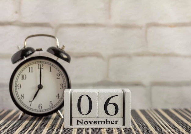 6 listopada na drewnianym kalendarzu obok budzika na ciemnym stole. Jeden dzień miesiąca jesiennego. Kalendarz na listopad. Jesień.