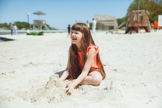 7-letnia dziewczynka bawi się w piasku na miejskiej plaży Wakacje i odpoczynek Zabawne, aktywne dziecko na plaży w letnie wakacje