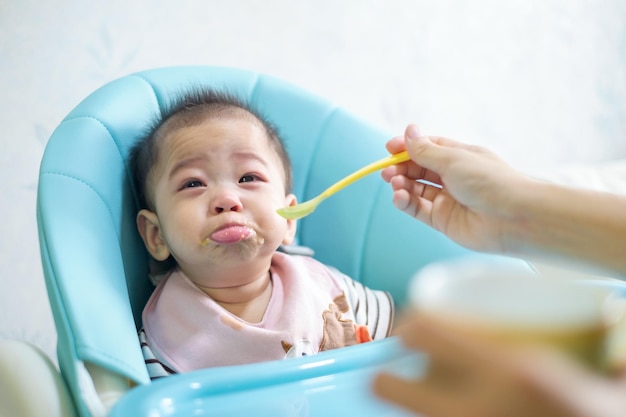 7 miesięczne dziecko smutna smutna buzia nieszczęśliwa siedzi na krześle Jest matka karmiąca śniadanie