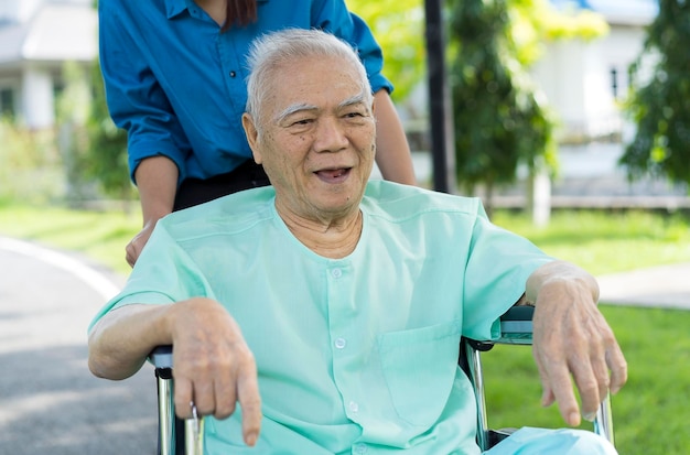 70-letni starszy starszy Azjata lub Taj na wózku inwalidzkim Śmiej się z asystentką pielęgniarki w parku