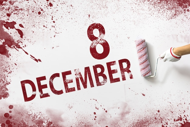 8 grudnia. Dzień 8 miesiąca, data kalendarzowa. Ręka trzyma wałek z czerwoną farbą i pisze datę w kalendarzu na białym tle. Miesiąc zimowy, koncepcja dnia roku.