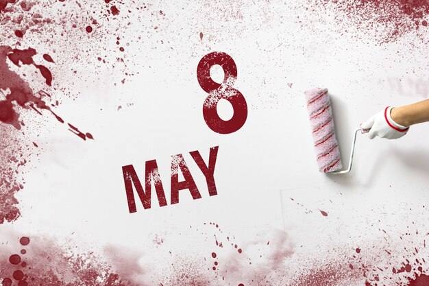8 maja. Dzień 8 miesiąca, data kalendarzowa. Ręka trzyma wałek z czerwoną farbą i pisze datę w kalendarzu na białym tle. Miesiąc wiosny, koncepcja dnia roku.