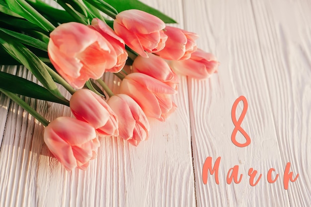 Zdjęcie 8 marca tekst na różowych tulipanach na białym rustykalnym drewnianym tle kartkę z życzeniami koncepcja zmysłowy delikatny dziewczęcy obraz wiosenne kwiaty w miękkim porannym świetle słonecznym