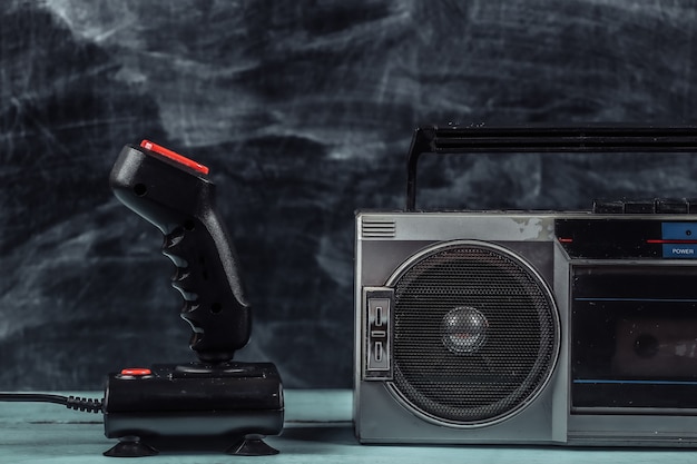 Zdjęcie 80s retro starej szkoły przenośny stereofoniczny magnetofon kasetowy i joystick na tle tablicy.