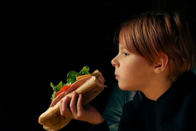 9-letni chłopiec je dużą kanapkę z bagietką