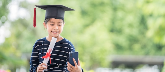 Zdjęcie absolwent dzieci z czapką maturalną i rolowanym świadectwem ukończenia szkoły, trzymający smartfona, aby zadzwonić