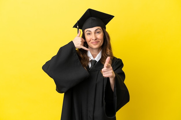 Absolwent uniwersytetu w średnim wieku, odizolowany na żółtym tle, wykonując gest telefonem i wskazując przód