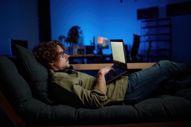 Administrator IT spoczywa na kanapie z laptopem leżącym na kanapie w nowoczesnej serwerowni. Nocna służba w koncepcji centrum danych