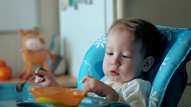 Adorable baby boy siedzi w krzesełku jedzenie puree zbóż z łyżką