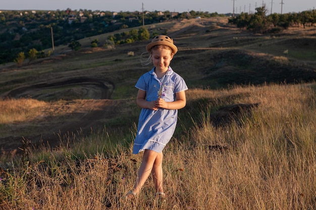 Adorable little girl w słomkowym kapeluszu niebieska chusta letnia sukienka w polu trawy wsi Dziecko z długimi blond warkoczami