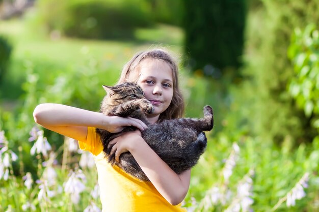 Adorale dziewczyna w żółtej sukience trzyma piękny kot w jej ręce. Dziecko i zwierzę na zewnątrz w letni dzień.