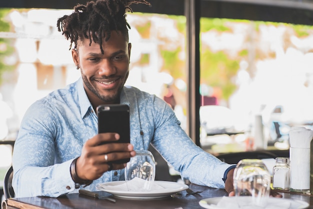 African American człowiek uśmiechający się podczas korzystania z telefonu komórkowego w restauracji.