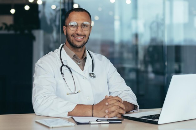 African american doctor portret człowieka pracującego w nowoczesnej klinice przy stole przy użyciu laptopa