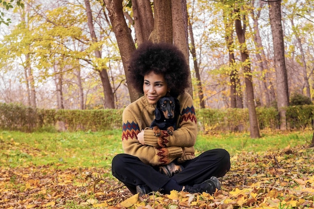 African American girl siedzi i przytulanie psa w parku jesienią