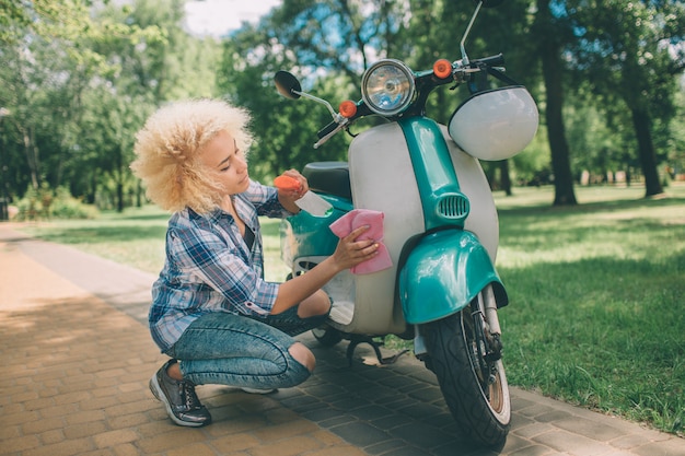 African American kobiet mycie skutera. Dziewczyna czyszczenia niebieski motorower lub motocykl.