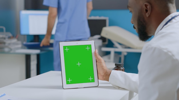 African American Lekarz Specjalista Patrząc Na Makiety Komputera Typu Tablet Z Zielonym Ekranem Chroma Key Z Izolowanym Wyświetlaczem. Terapeuta Mężczyzna Pracujący W Leczeniu Opieki Zdrowotnej W Biurze Szpitala. Usługi Medyczne