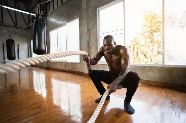 African sport człowiek robi liny bojowe treningu funkcjonalnego na siłowni. Zdeterminowany trener robi fale na linach podczas ćwiczeń siłowych. Sportowiec ćwiczący z liną bojową na siłowni przemysłowej.