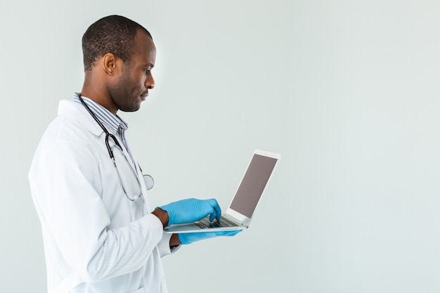 Afro-amerykański lekarz stojący przed białą ścianą i surfowanie po Internecie