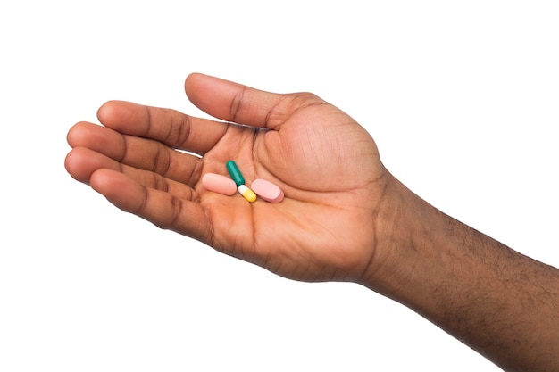 Afro-amerykańskie ręce trzymając pigułkę w jednej ręce i talerz tabletek w drugiej na białym tle. Opieka zdrowotna, koncepcja leczenia
