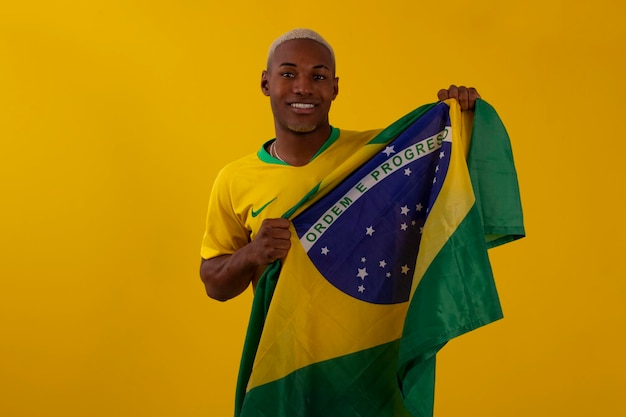 Afro Brazylijczyk kibic brazylijskiej drużyny piłkarskiej w pucharze 2022 z flagą Brazylii i wyrazem twarzy