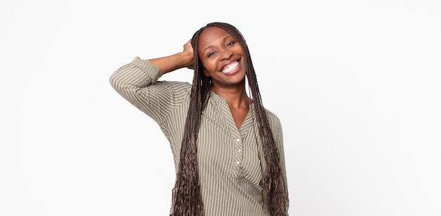 Afro czarna dorosła kobieta uśmiechająca się radośnie i od niechcenia, biorąca rękę w głowę z pozytywnym, szczęśliwym i pewnym siebie spojrzeniem