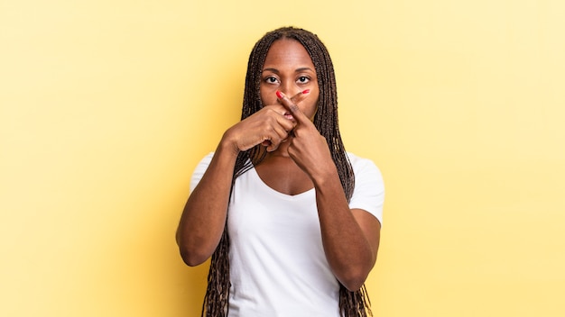 Afro czarna ładna kobieta wyglądająca na poważną i niezadowoloną z dwoma palcami skrzyżowanymi z przodu w odrzuceniu, proszącą o ciszę