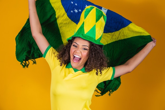 Zdjęcie afro dziewczyna kibicująca ulubionej brazylijskiej drużynie, trzymająca flagę narodową na żółtym tle.