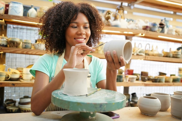 Afro Kobieta robi ceramikę w warsztacie Kształtowanie mokrej gliny na kole garncarskim