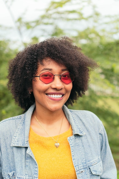 Afro kobieta uśmiecha się, pozując z rękami skrzyżowanymi na zielonym naturalnym tle