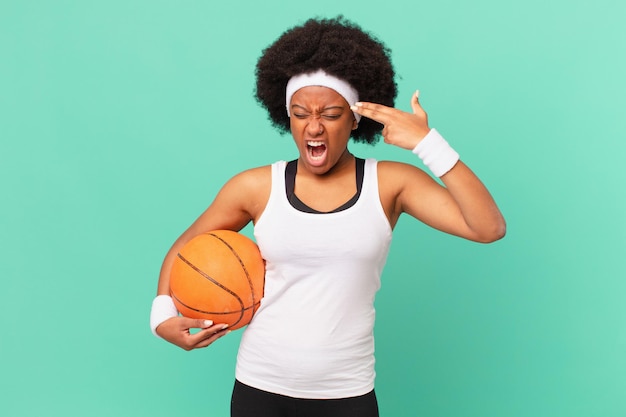 Afro kobieta wyglądająca na niezadowoloną i zestresowaną, samobójczy gest robiący znak pistoletu ręką, wskazujący na głowę. koncepcja koszykówki