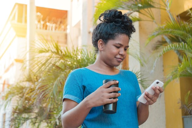 Afro kobieta z termosem z kawą i sprawdzaniem swojego telefonu komórkowego.