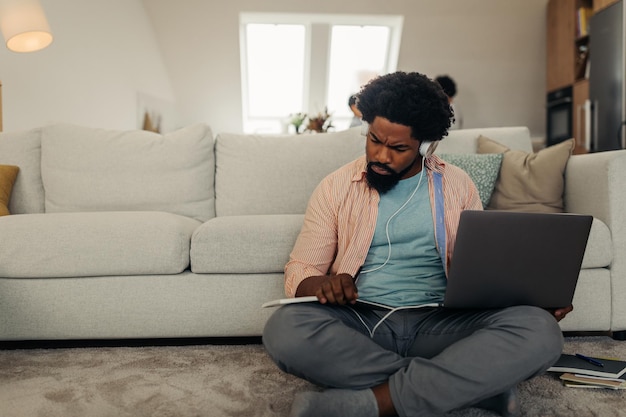 Afro mężczyzna pracujący w domu w przytulnym salonie przy użyciu technologii