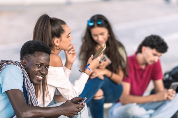 Afro mężczyzna siedzący obok zróżnicowanej grupy przyjaciół korzystających z telefonu komórkowego