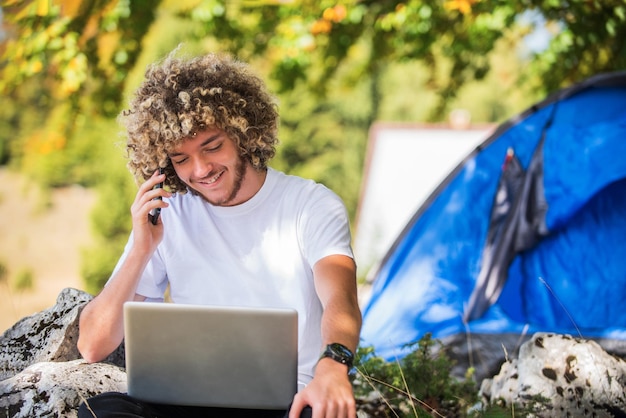 Afro mężczyzna siedzi na łonie natury i używa smartfona i laptopa do spotkania online