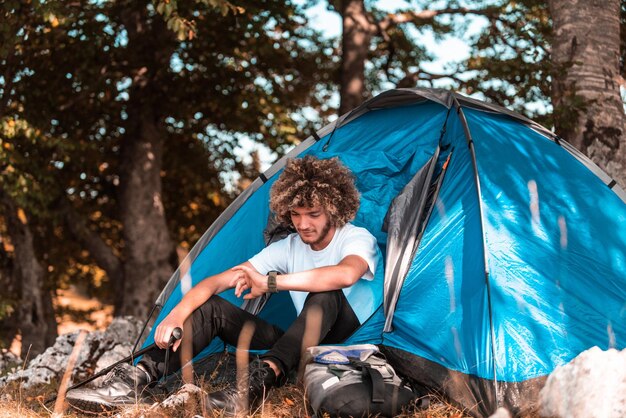 Afro mężczyzna używa inteligentnego zegarka, siedząc przed namiotem alpinistycznym. Wysokiej jakości zdjęcie