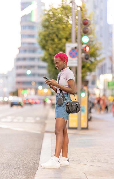 Afro młoda kobieta stojąca na ulicy za pomocą telefonu komórkowego