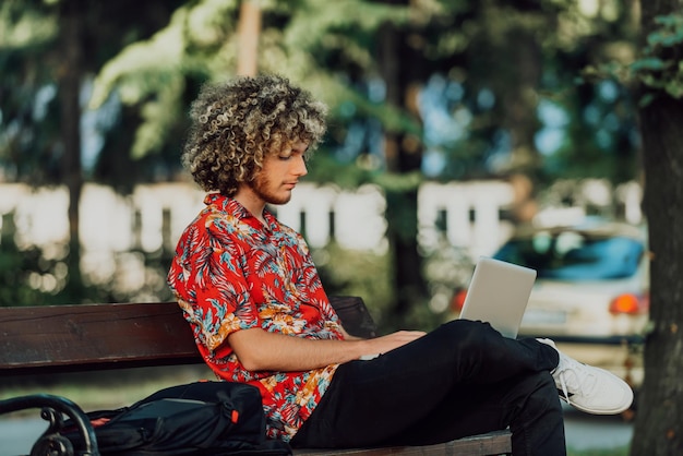 Afro nastolatek używa laptopa do spotkania online, siedząc na ławce w parku