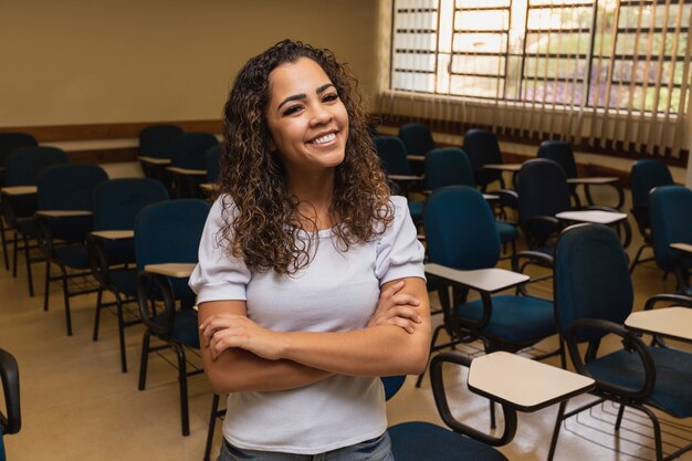 Afro Student W Klasie Z Rękami Skrzyżowanymi Patrząc Na Kamery Uśmiecha Się. Młody Student Z Klasą W Tle.